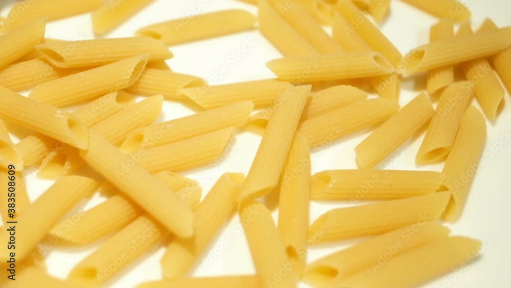 Uncooked penne pasta falling on white surface slow motion,kitchen food background Uncooked penne pasta falling on white surface slow motion,kitchen food background