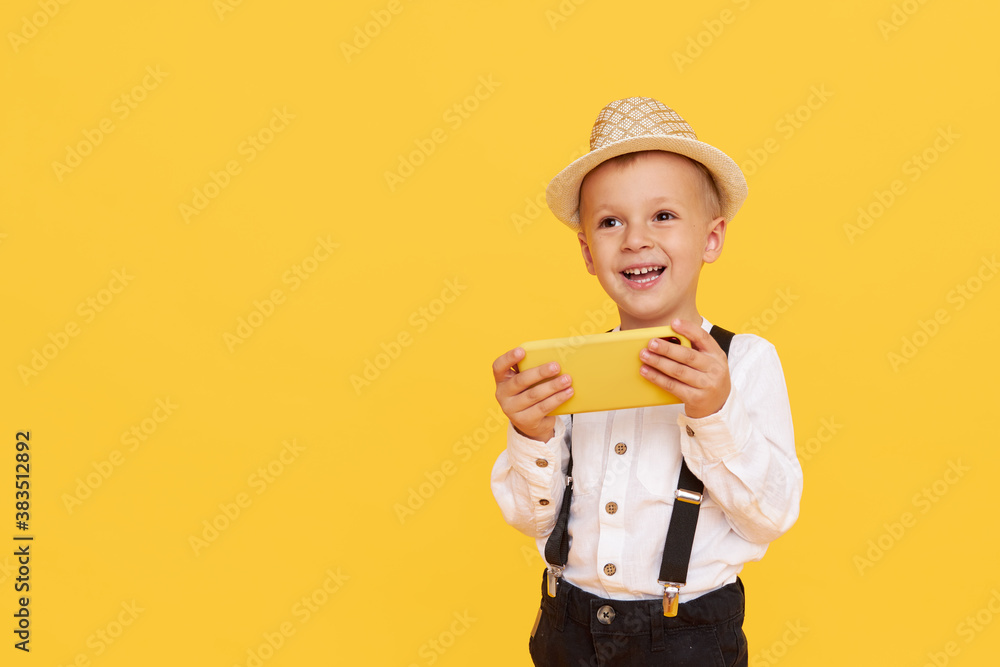 Cute smilling child boy with smartphone on yellow background. Advertising of educational applications on a mobile phone for children. Funny face. Cute smilling child boy with smartphone on yellow background. Advertising of educational applications on a mobile phone for children. Funny face.