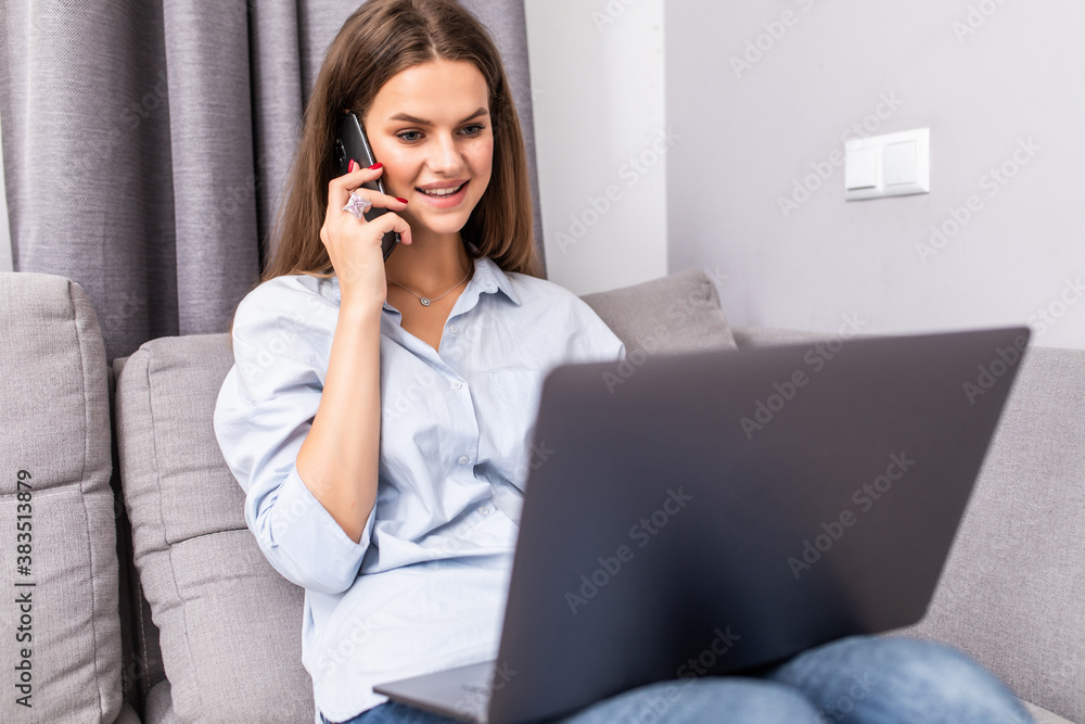 Young woman using laptop and cellphone on sofa at home