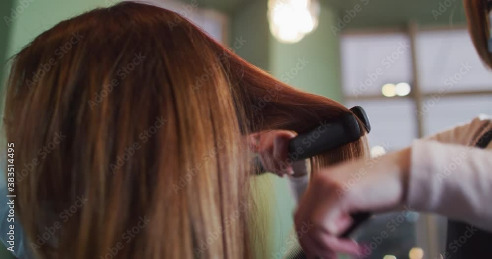 Female hairdresser straightening hair of female customer at hair salon Female hairdresser straightening hair of female customer at hair salon