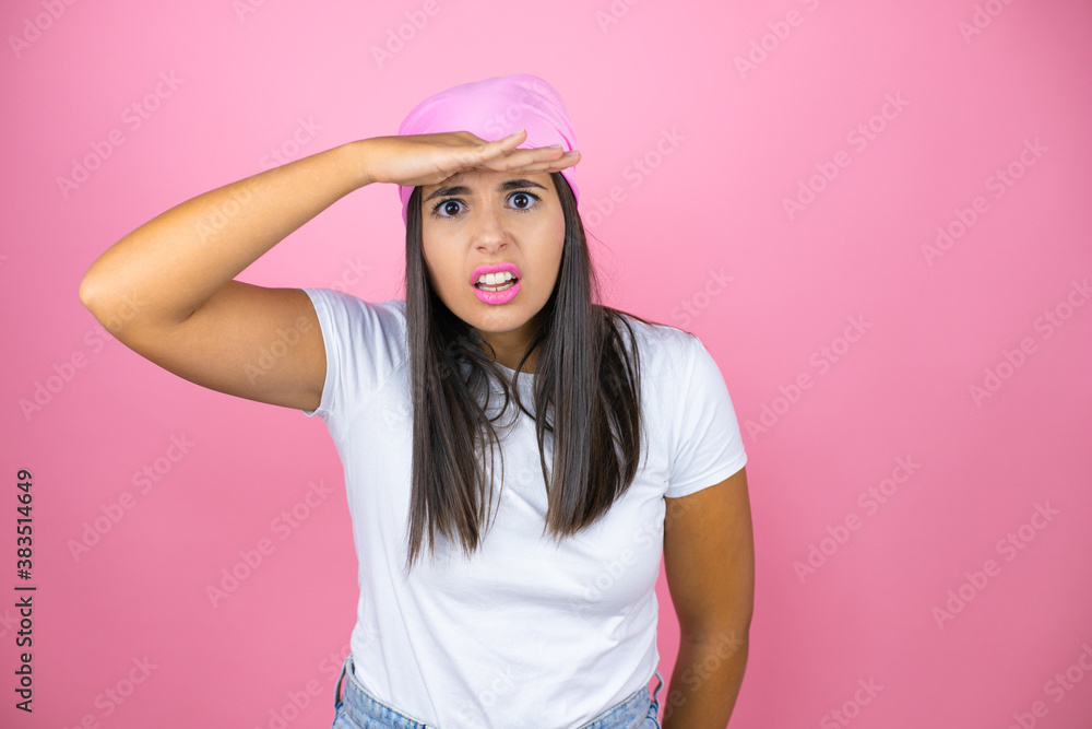 Young beautiful woman wearing pink headscarf over isolated pink background very happy and smiling looking far away with hand over head. searching concept. Young beautiful woman wearing pink headscarf over isolated pink background very happy and smiling looking far away with hand over head. searching concept.