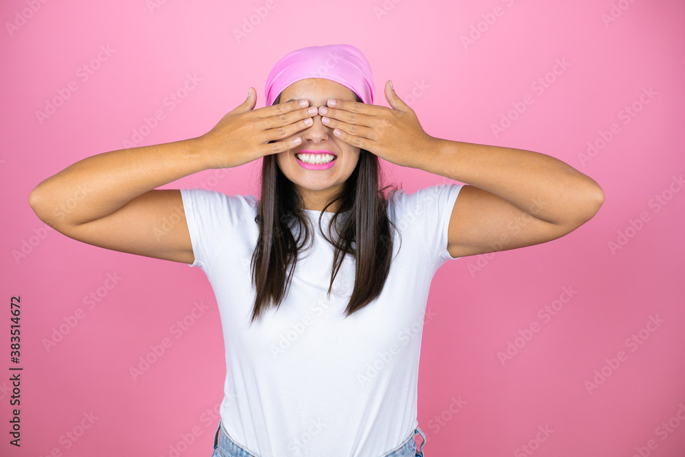 Young beautiful woman wearing pink headscarf over isolated pink background covering eyes with hands smiling cheerful and funny. Blind concept. Young beautiful woman wearing pink headscarf over isolated pink background covering eyes with hands smiling cheerful and funny. Blind concept.