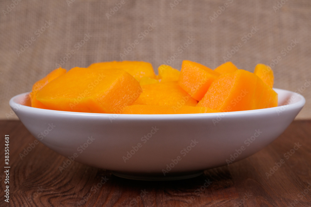 Pieces of pumpkin in the bowl at the wooden table and sackcloth background. Pieces of pumpkin in the bowl at the wooden table and sackcloth background.
