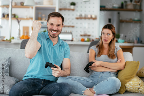 Husband and wife playing video game with joysticks in living room. Loving couple are playing video games at home.