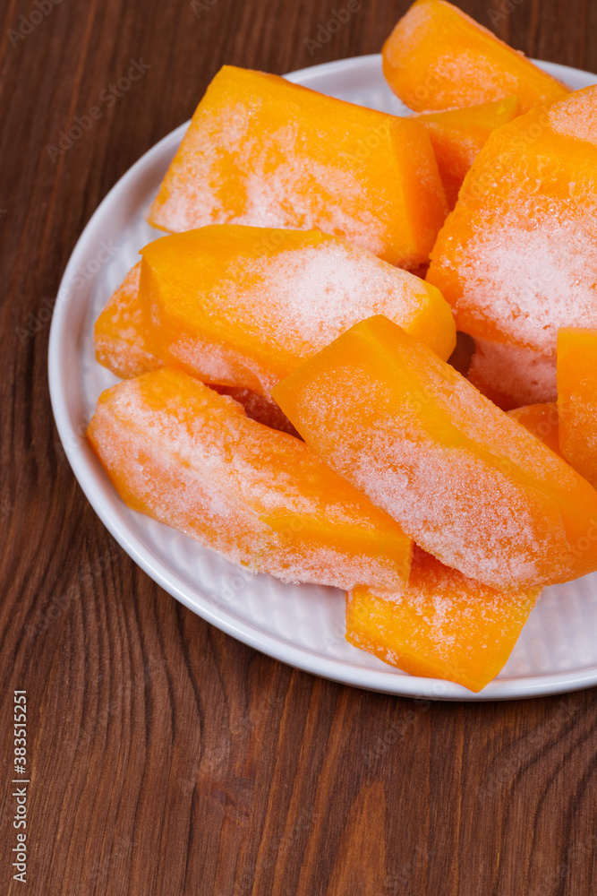 Frozen pieces of pumpkin on the plate at the wooden table.
