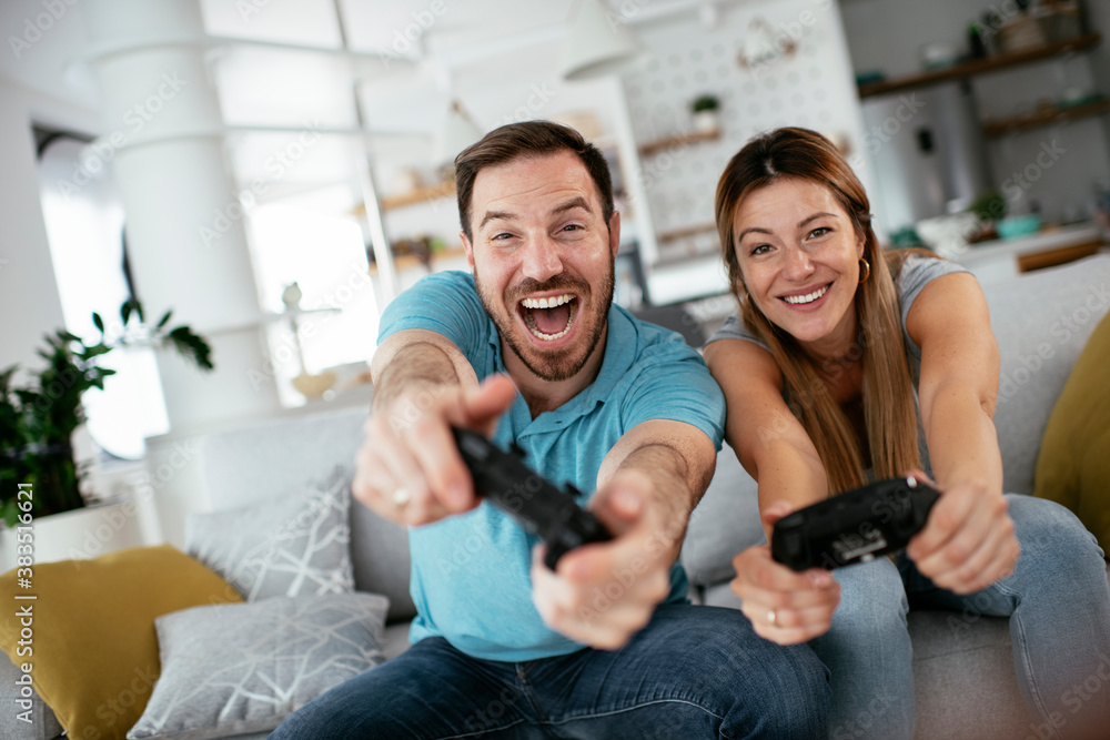 Husband and wife playing video game with joysticks in living room. Loving couple are playing video games at home. Husband and wife playing video game with joysticks in living room. Loving couple are playing video games at home.