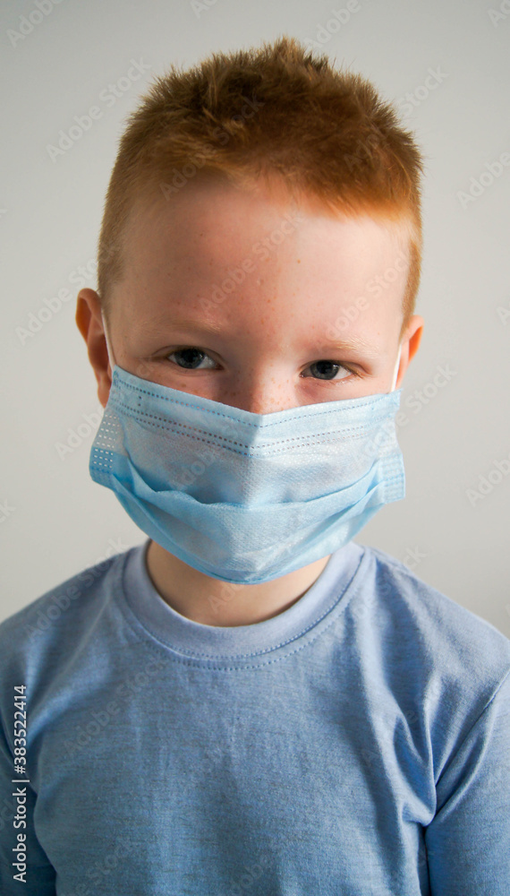 Ginger red head child  in a protective mask on the white background. Kid using the medical face mask for protection during the covid-19.