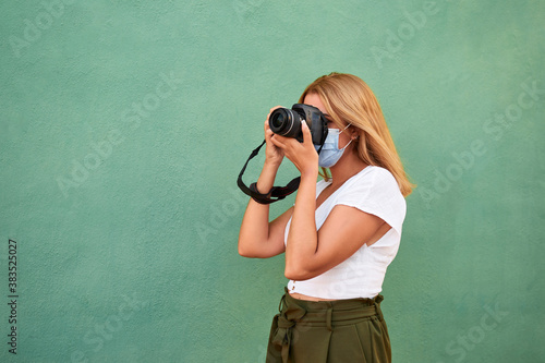 Vászonkép Young woman with a mask and a camera on a green background