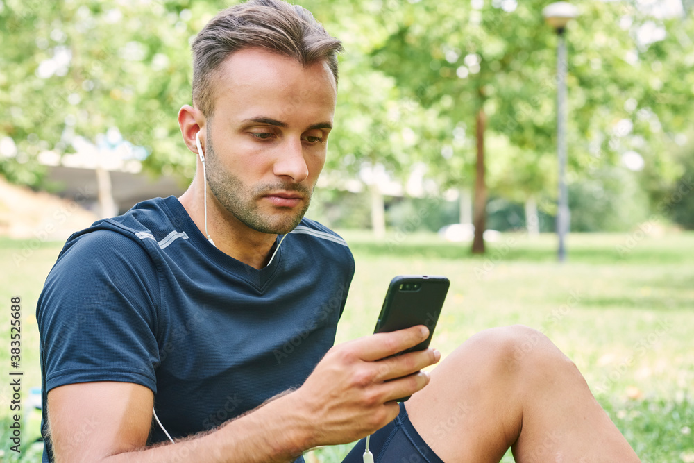 Man with his smart phone sitting on the grass in a park after training. Healthy and healthy life. Health and sport concept. Man with his smart phone sitting on the grass in a park after training. Healthy and healthy life. Health and sport concept.