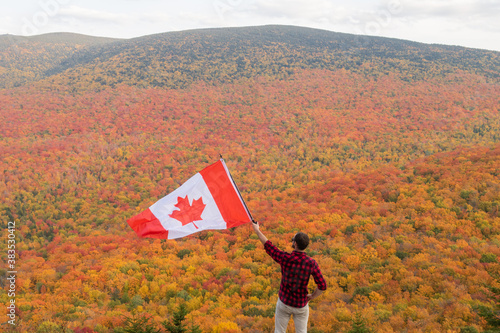 Autumnal view of a man with a lumberjack shirt holding a Canadian flag in the Mont-Megantic national park, Canada photo