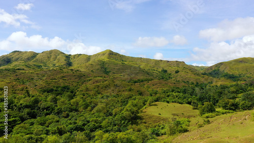 Hills with green grass and blue sky with white puffy clouds. Beautiful landscape on the island of Luzon, aerial view.