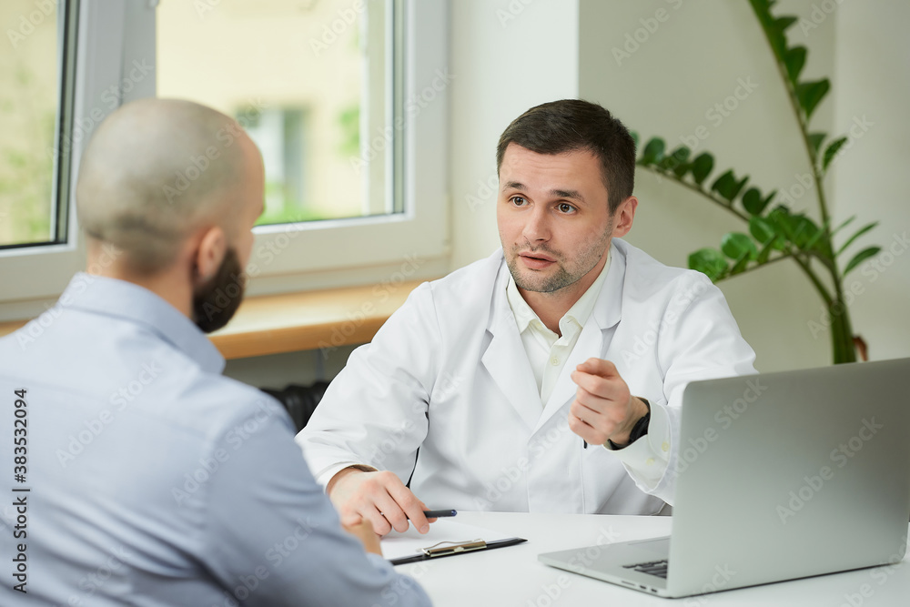 Obraz premium A caucasian doctor in a white lab coat is describing and demonstrating the treatment to a bald male patient in a hospital. A man with a beard at an appointment in a doctor's office.
