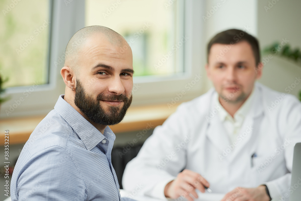 A bald male patient is smiling near a caucasian doctor in a white lab coat in a hospital. A man with a beard at an appointment in a doctor's office. A bald male patient is smiling near a caucasian doctor in a white lab coat in a hospital. A man with a beard at an appointment in a doctor's office.