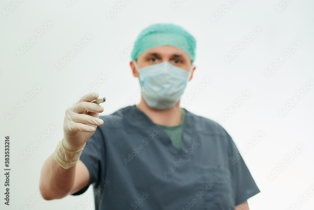 A photo of a surgeon in scrubs with a focus on a scalpel in a hospital. White background behind a doctor who wears a surgical shirt, disposable gloves, a medical face mask, and a scrub cap. A photo of a surgeon in scrubs with a focus on a scalpel in a hospital. White background behind a doctor who wears a surgical shirt, disposable gloves, a medical face mask, and a scrub cap.
