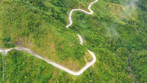 Mountain curve road passing along the slopes of mountains and hills covered with green forest and vegetation. Philippines, Luzon. Mountains covered by rainforest, aerial view.
