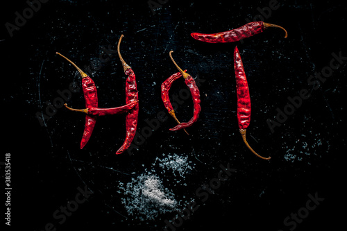 HOT written on a black surface with the help of some red hot chilies. Top shot of red hot chilies making hot word.