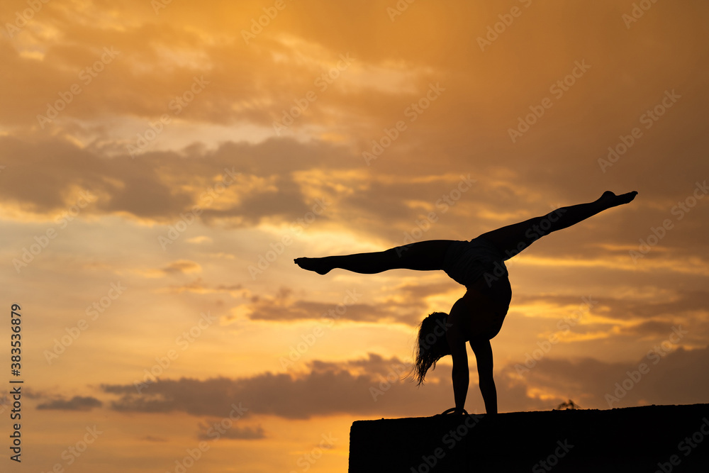 Flexible girl doing exercise on sky background during dramatic sunset