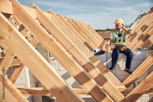 Hard-working builder sitting near a wooden roof frame