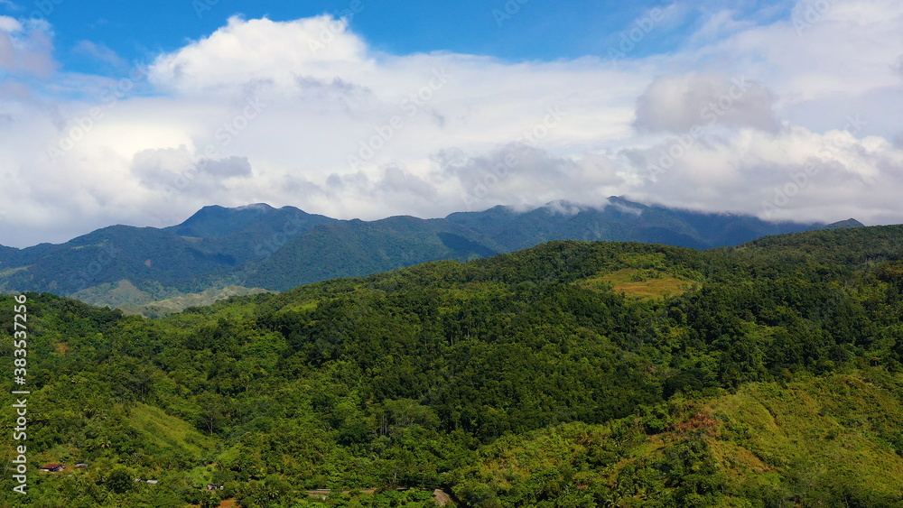 Hills and mountains covered with green grass and rainforest against a background of blue sky and clouds. Philippines, Luzon. Summer landscape.