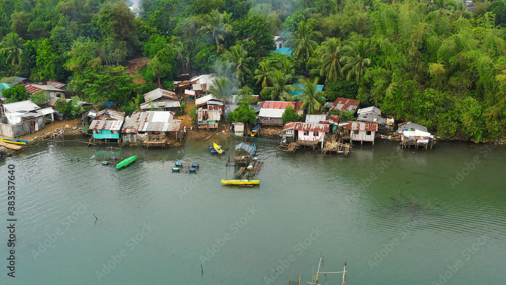 Fishing village with boats and slums with wooden houses, aerial drone. Houses community standing in water in fishing village. Luzon, Philippines.
