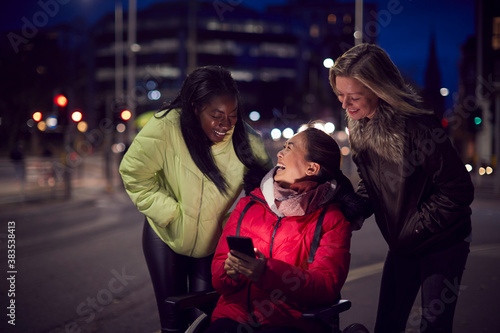 Woman In Wheelchair Having Night Out With Friends In City Ordering Taxi Using Mobile Phone App