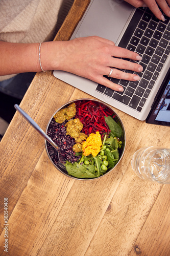 Close Up Businesswoman Working On Laptop Whilst Eating Vegan Lunch At Wooden Table