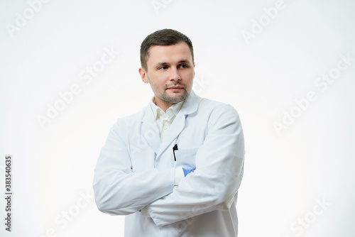 A male caucasian doctor in a white lab coat and blue disposable medical gloves is staying crossed his arms over his chest. A scientist is isolated over white background. © Roman Tyukin