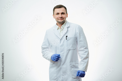 Obraz na płótnie A kind male caucasian doctor in a white lab coat and blue disposable medical gloves is posing with a smile. A scientist is isolated over white background. w salonie