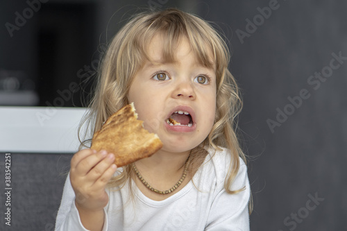 A little girl sits with her mouth open at the kitchen table and eats pizza.