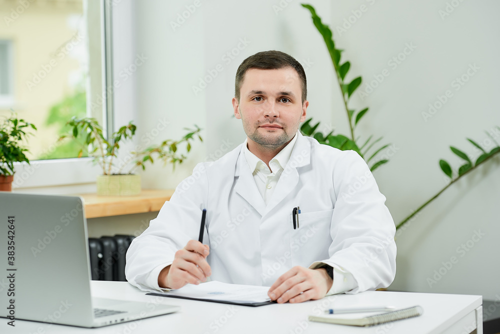 A caucasian doctor in a white lab coat is posing near a laptop in a hospital. A male therapist is waiting for a patient in a doctor's office.