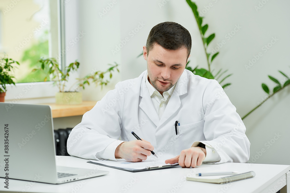 A caucasian doctor in a white lab coat is filling out a patient card with a diagnosis near a laptop in a hospital. A therapist is waiting for a patient in a doctor's office.
