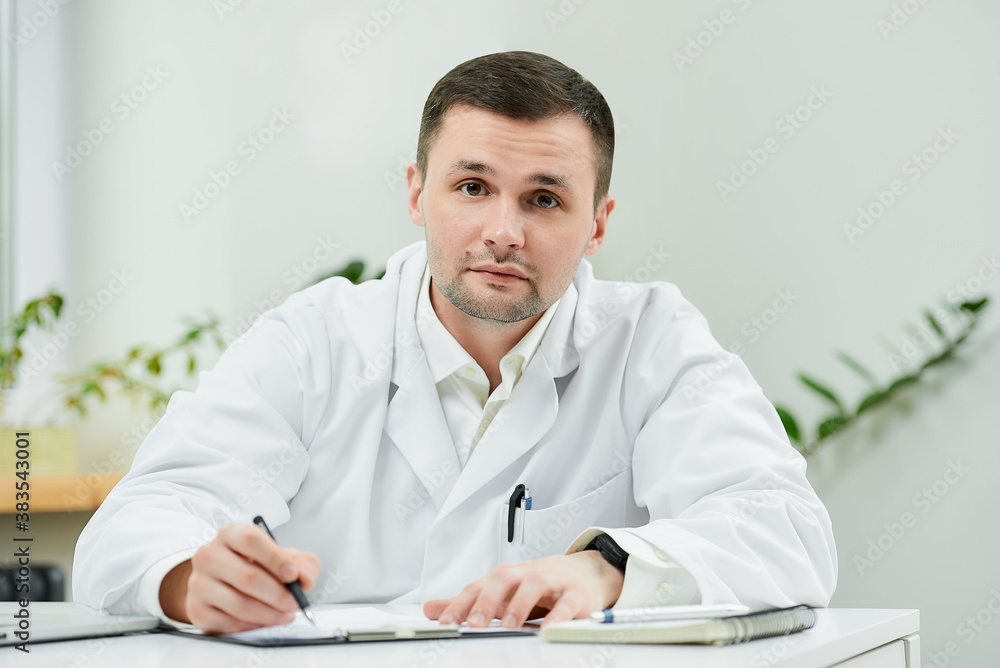 A serious caucasian doctor in a white lab coat is sitting at his desk and distracted from examining the patient’s medical history in a hospital. A therapist near a laptop in a doctor's office. A serious caucasian doctor in a white lab coat is sitting at his desk and distracted from examining the patient’s medical history in a hospital. A therapist near a laptop in a doctor's office.