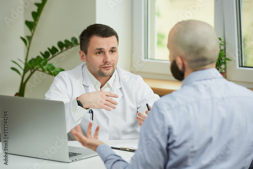 Photography A caucasian doctor in a white lab coat is sitting at a desk and arguing about the treatment of a bald male patient in a hospital