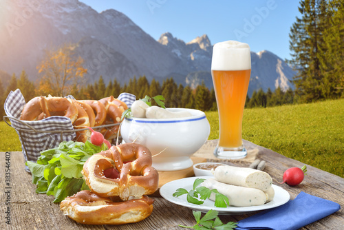 Deftiges, bayerisches Weißwurstfrühstück in den Bergen – Hearty Bavarian breakfast with veal sausages, fresh pretzels and a wheat beer outside in the nature near Garmisch-Partenkirchen