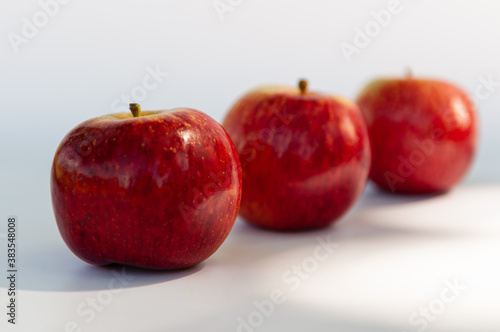 Three red apples with focus on the foreground and blur background on a white table. Selective focus