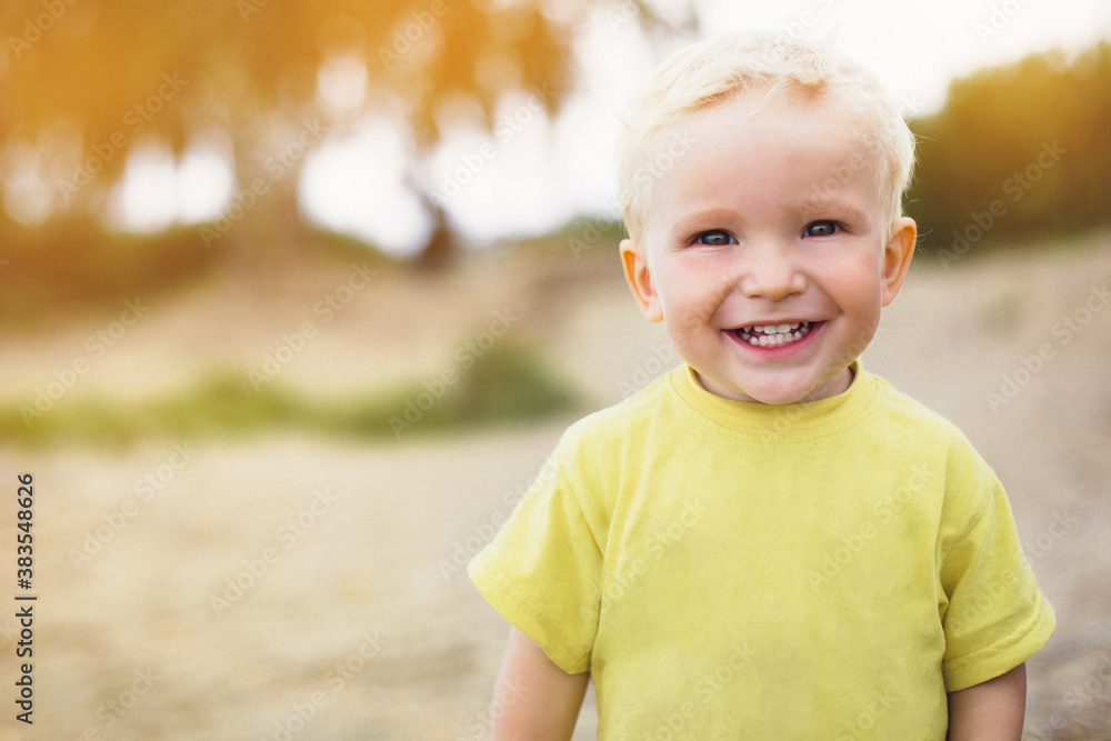 Close-up portrait of a 3 year old boy on a background of nature and sunset. Blond-haired kid in a yellow plain t-shirt. Happy smiling baby. Close-up portrait of a 3 year old boy on a background of nature and sunset. Blond-haired kid in a yellow plain t-shirt. Happy smiling baby.