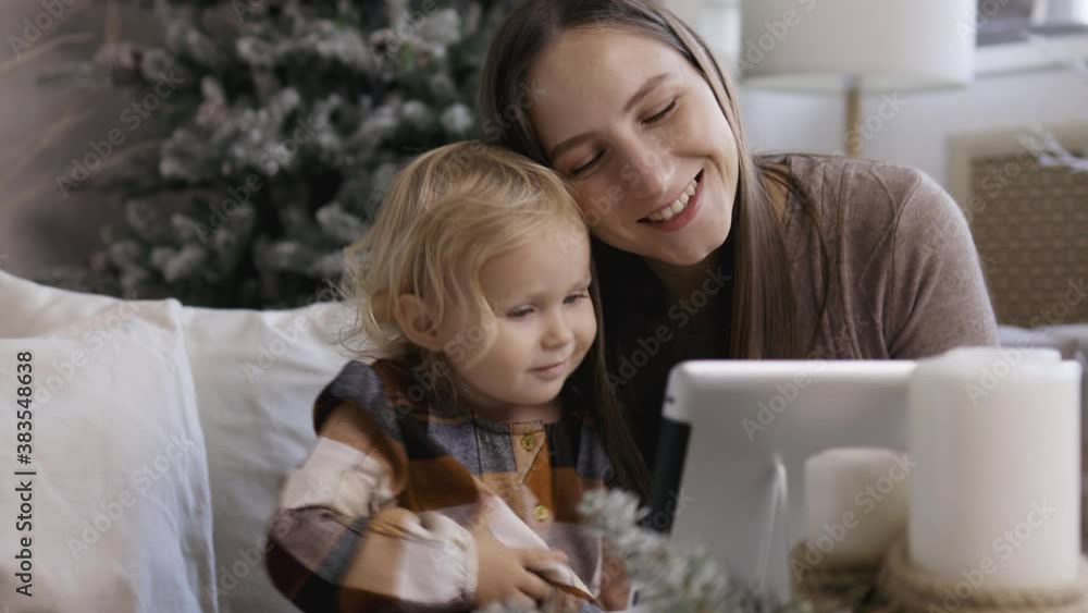Mother and daughter make video call via pad on Christmas morning. Young mom with her little daughter congratulate their relatives a happy new yaer. Mother and daughter make video call via pad on Christmas morning. Young mom with her little daughter congratulate their relatives a happy new yaer.