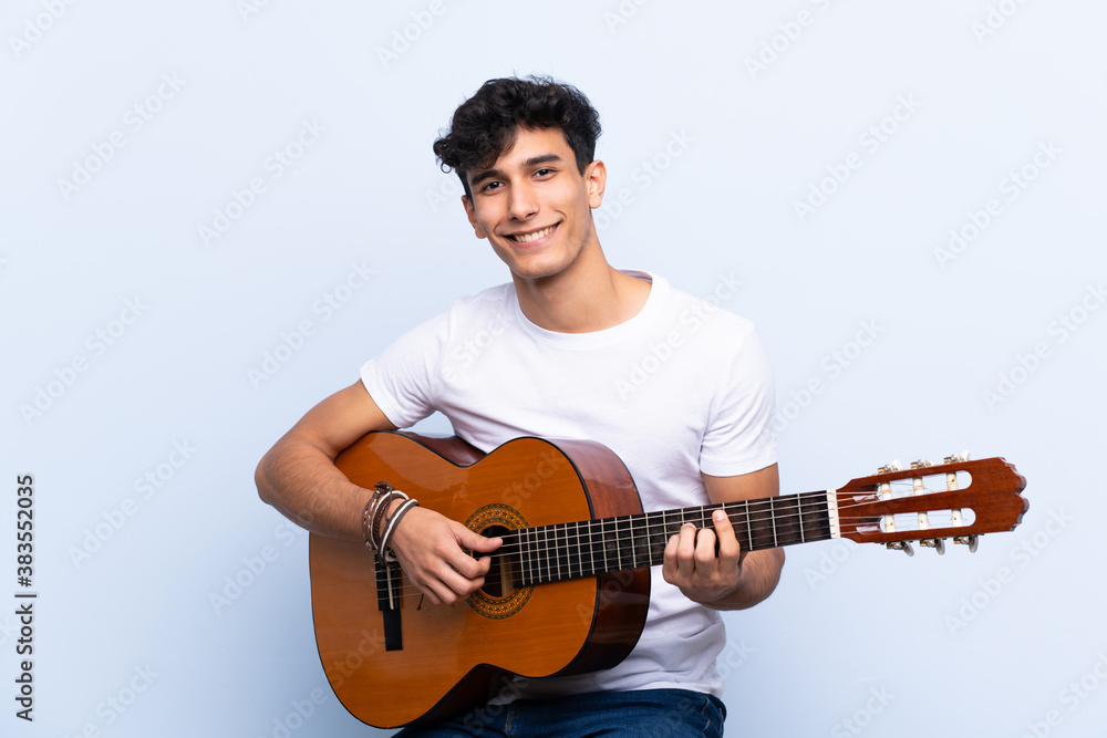 Obraz premium Young Argentinian man with guitar over isolated blue background showing ok sign with fingers