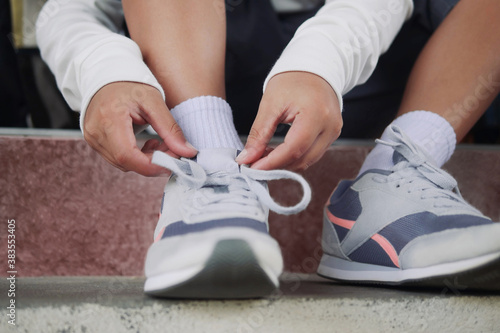 Schoolboy in casual clothing tying shoelaces on sneakers getting ready for school or traveling.
