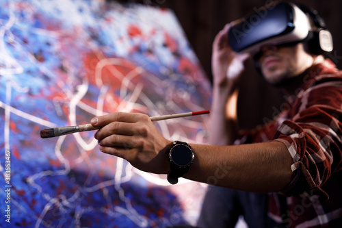 Talented male artist wearing virtual reality headset in creative modern studio. Artist works on abstract oil painting. Abstract Modern Art.