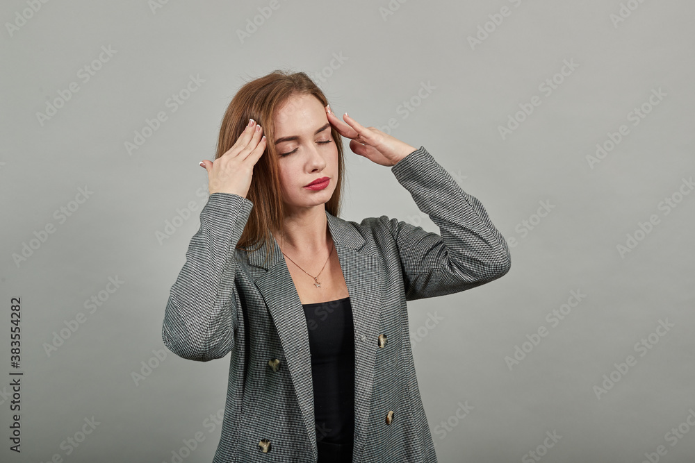 Headache grimacing pain holds the back of neck indicating location. Fatigue during workaholism labor. Young attractive woman, dressed gray jacket, with green eyes, light brown hair, background Headache grimacing pain holds the back of neck indicating location. Fatigue during workaholism labor. Young attractive woman, dressed gray jacket, with green eyes, light brown hair, background