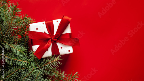 Christmas composition on a red background with a white gift box, with a red ribbon with fir branches, toys, copy space for your congratulations	