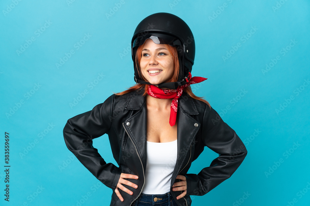Teenager biker girl isolated on blue background posing with arms at hip and smiling Teenager biker girl isolated on blue background posing with arms at hip and smiling