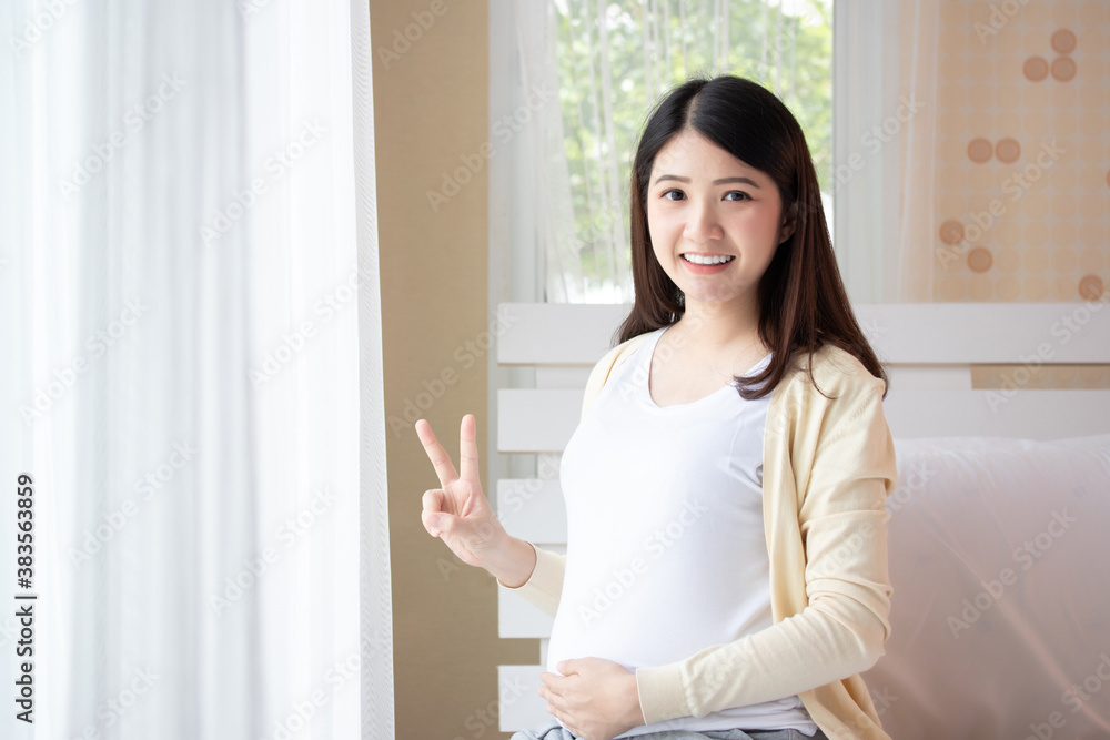 Young beautiful pregnant woman sitting and touching belly near the window in bedroom. Pregnancy, motherhood, people and expectation concept. Young beautiful pregnant woman sitting and touching belly near the window in bedroom. Pregnancy, motherhood, people and expectation concept.