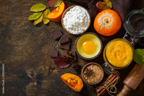 Seasonal food background - ingredients for autumn baking (pumpkin puree, eggs, flour, chocolate, sugar and spices) on a wooden table. Top view flat lay background. Copy space.