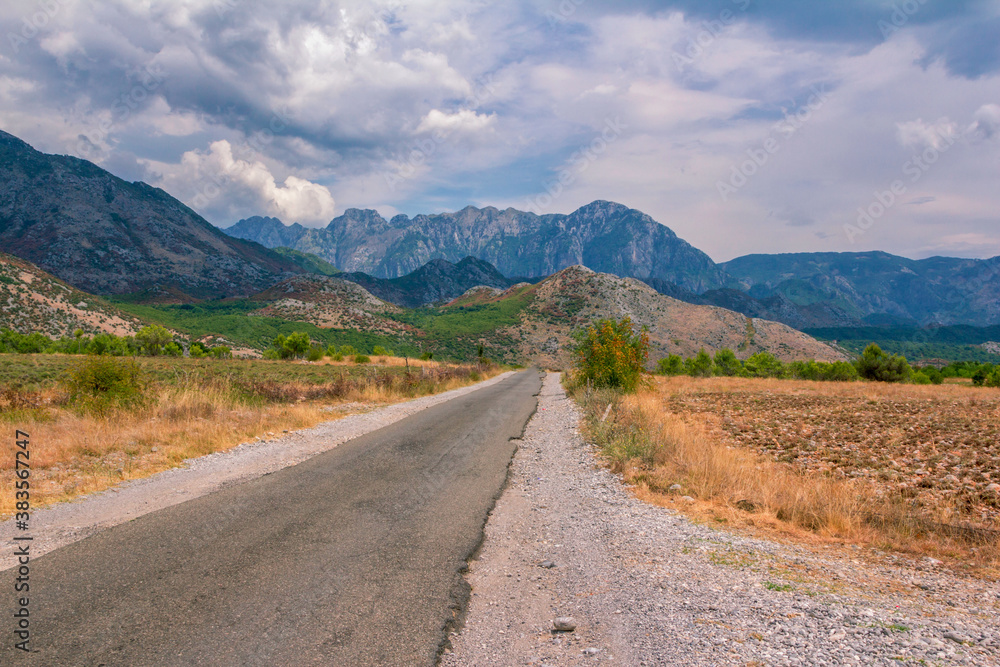 Summer landscape – valley and road in Albanian mountains, agricultural fields and gray  clouds on the sky.