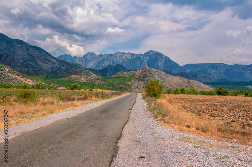 Summer landscape – valley and road in Albanian mountains, agricultural fields and gray clouds on the sky.
