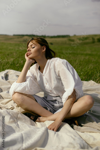 Nice picnic on the grass. Young beautiful woman in the middle of green field. Summer landscape, good weather. Windy day with sun and clouds. Cotton white suit eco style.  © Дарья Чачева