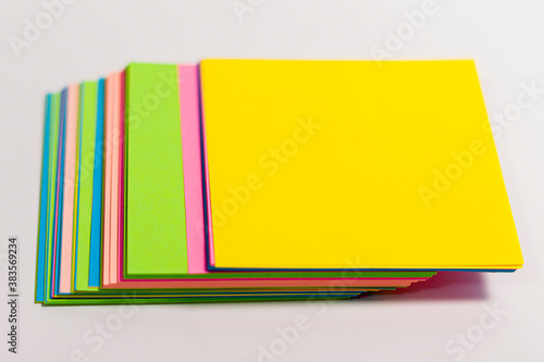 Sheets of paper of different colors are arranged in the center of the frame in a column on a white surface.