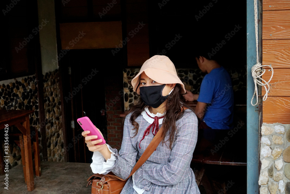 Obraz premium woman wear face mask holding mobile phone sit away from others, social distancing, covid-19 prevention